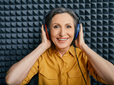Hearing loss treatment. Positive mature woman wearing audiometry headphones while hearing test and audiogram in special audio room
