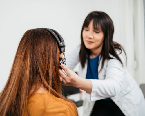 Beautiful middle age brunette woman receiving medical treatment. Hearing aid checkup. Otolaryngology.