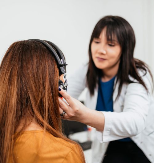 Beautiful middle age brunette woman receiving medical treatment. Hearing aid checkup. Otolaryngology.