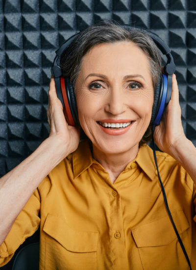 Hearing loss treatment. Positive mature woman wearing audiometry headphones while hearing test and audiogram in special audio room