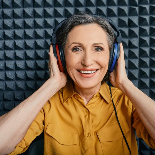 Hearing loss treatment. Positive mature woman wearing audiometry headphones while hearing test and audiogram in special audio room
